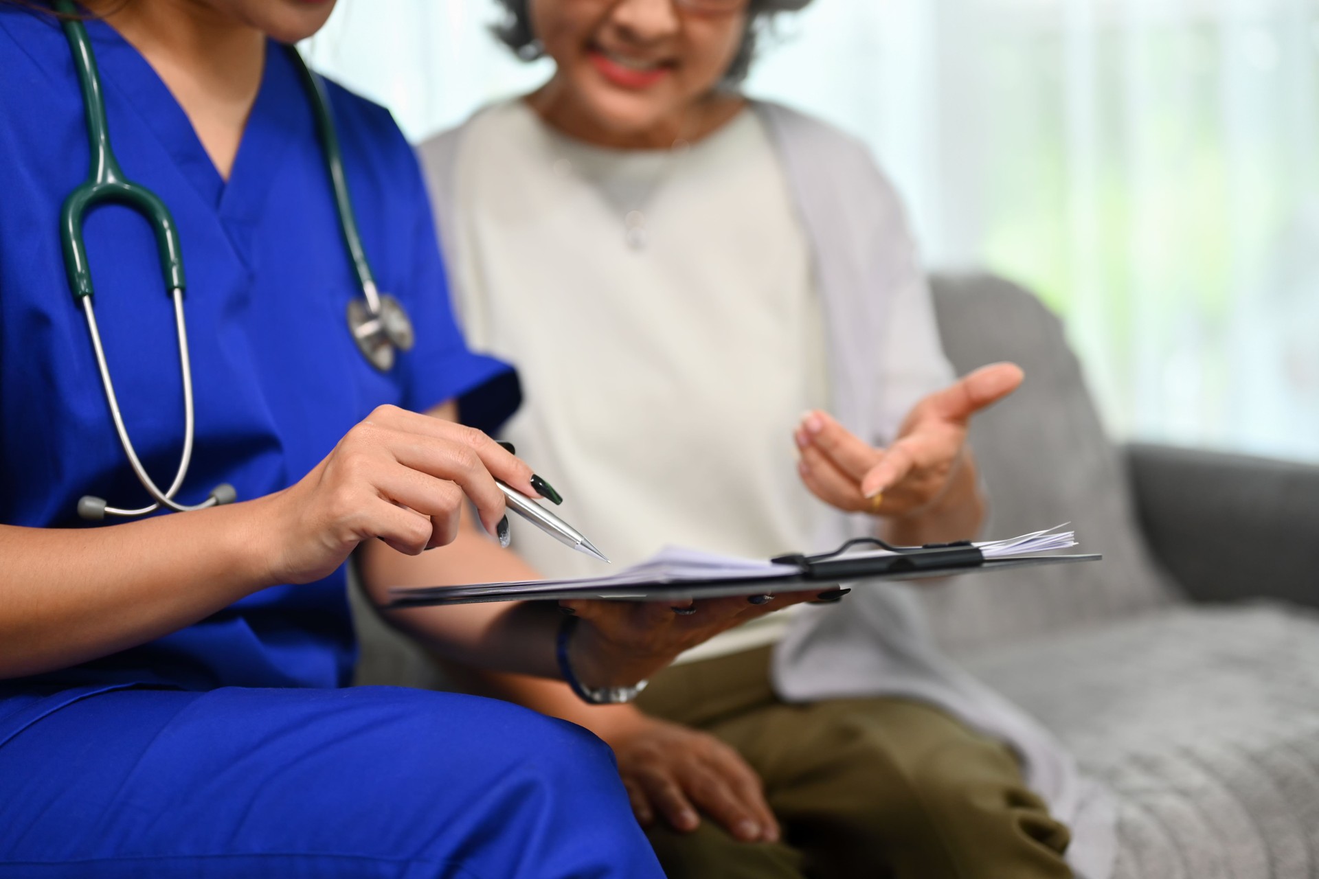 Healthcare worker pointing at clipboard showing health test results to senior patient during home visit.